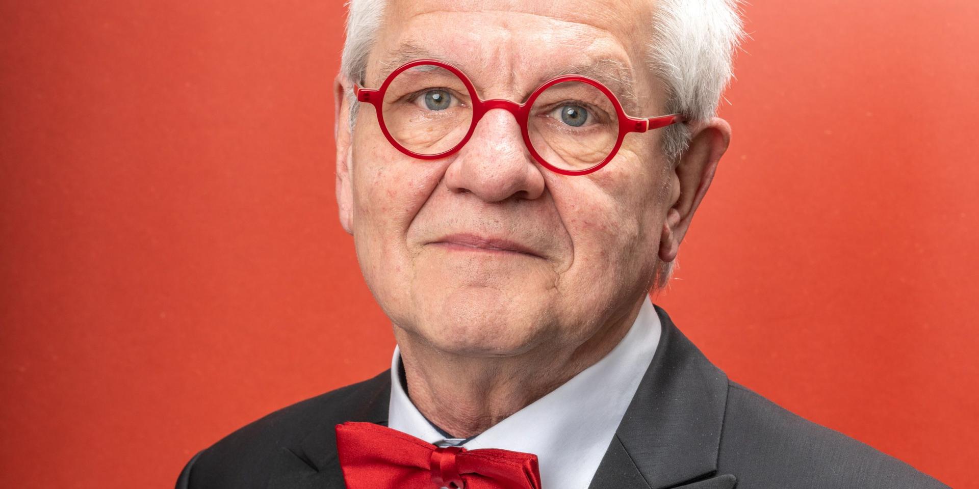 Reinhard Goebel in primo piano accenna un sorriso indossando occhiali e farfallino rossi