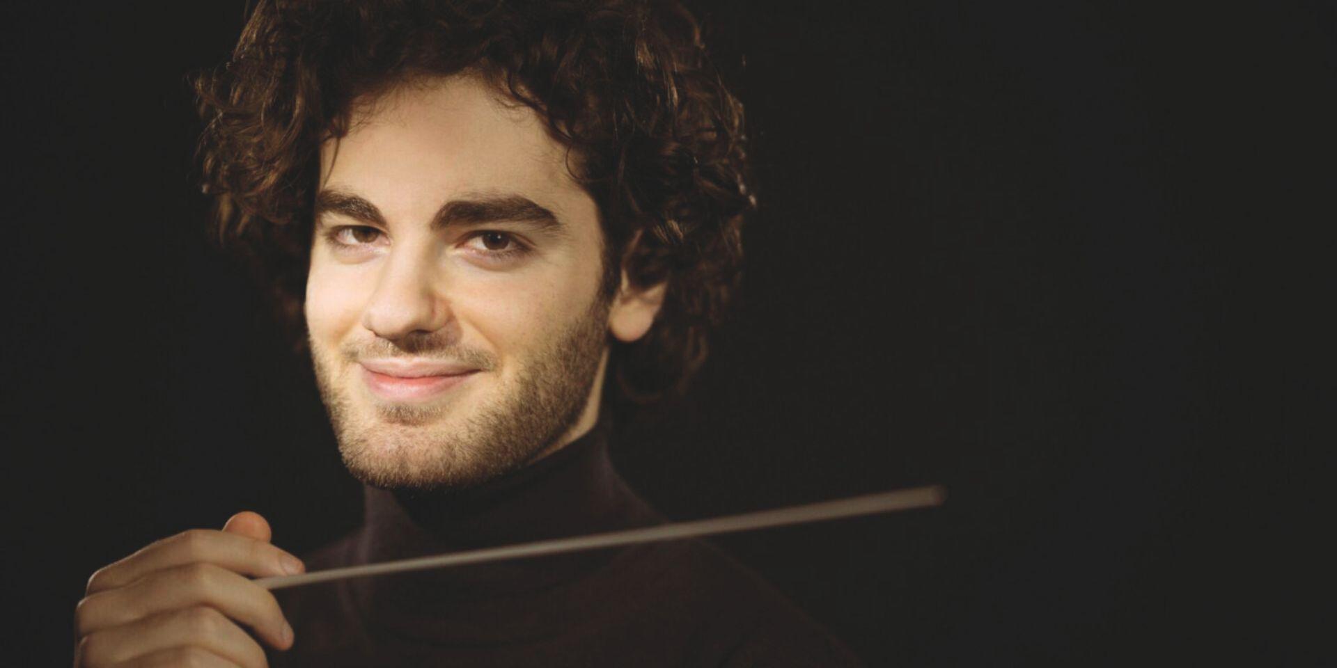 A close-up portrait of conductor Emmanuel Tjeknavorian against a black background.