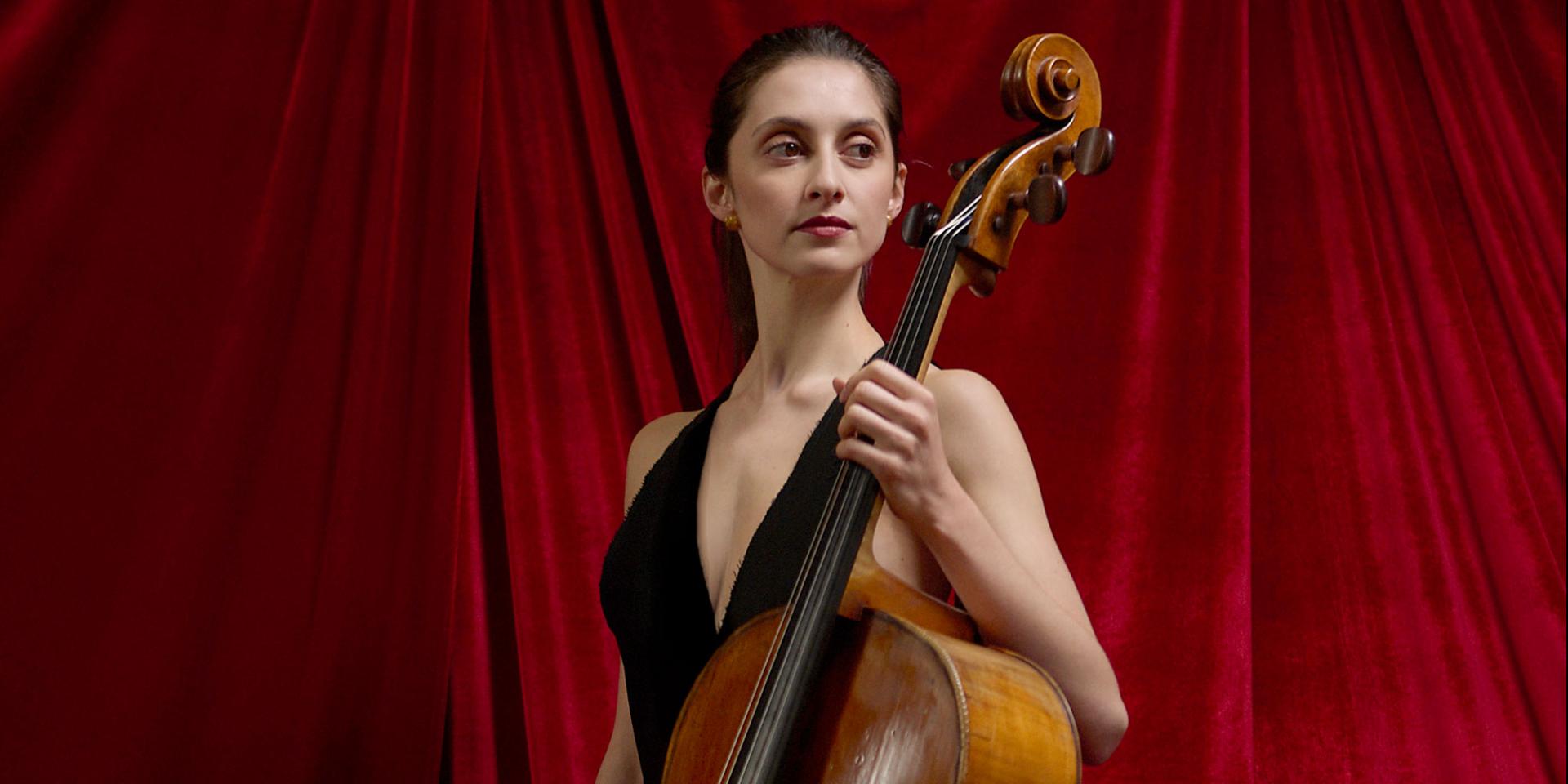 Una giovane donna con abito nero tiene in mano un violoncello con sguardo fiero 