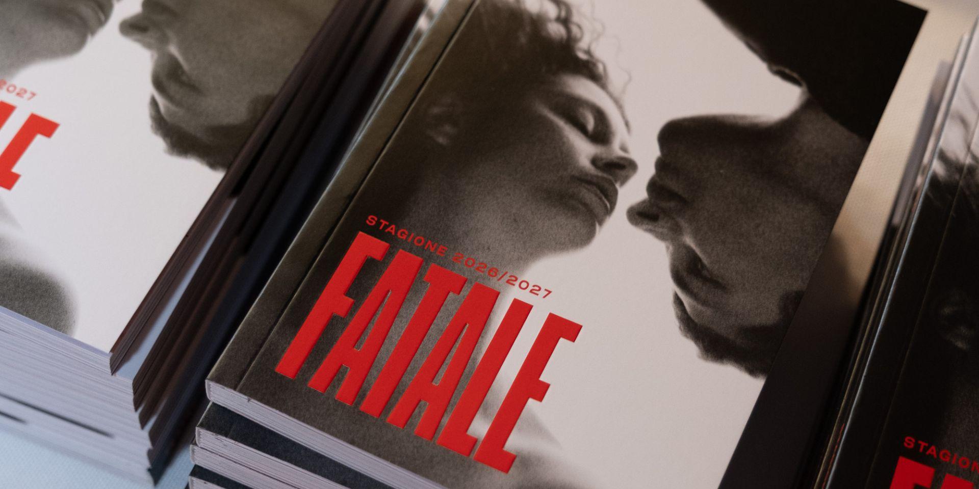 Stacks of brochures for the 2026/2027 Teatro Regio Season, featuring a cover with two black-and-white faces leaning in almost to the point of touching, topped by the word “Fatale” in large red letters.