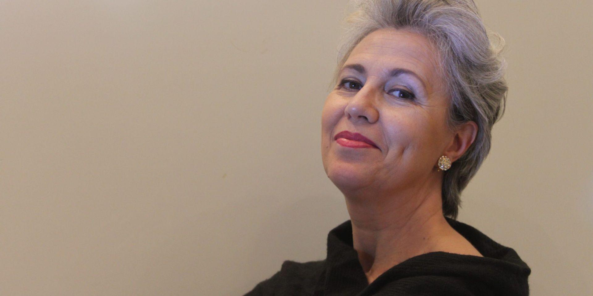 Contralto with short silver-grey hair, red lips, and a black dress, portrayed in a three-quarter view with a serene gaze directed upwards against a neutral beige background
