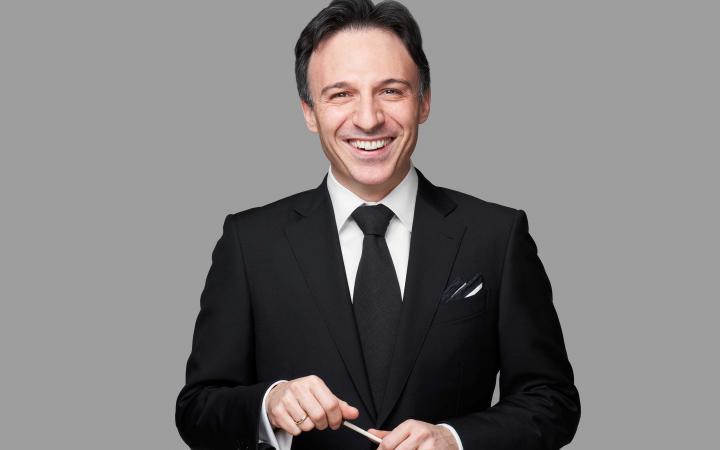 Umberto Clerici sorridente in abito e cravatta neri con la bacchetta in mano