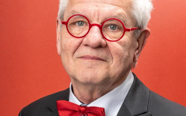 Reinhard Goebel in primo piano accenna un sorriso indossando occhiali e farfallino rossi