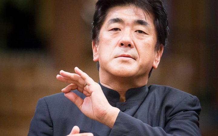 Yutaka Sado ripreso frontalmente mentre dirige, indossa una giacca grigio scuro alla coreana