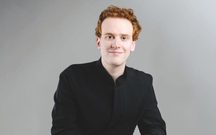 A waist-up portrait of conductor Nicolò Umberto Foron against a neutral gray background.