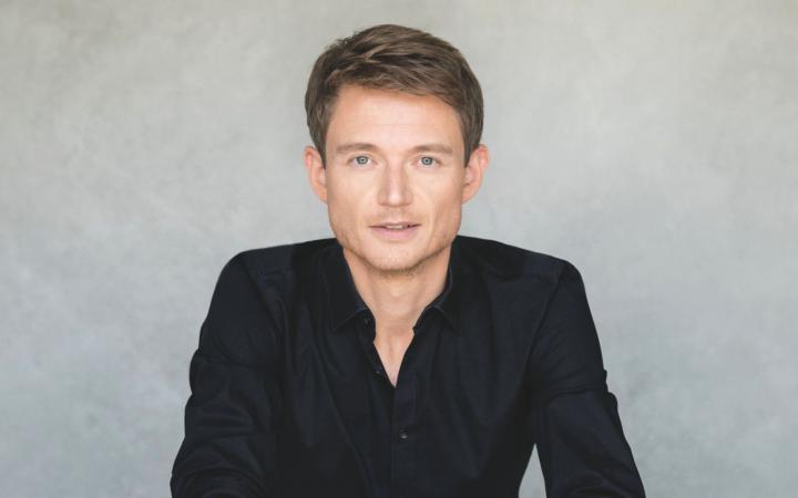 A waist-up portrait of conductor Felix Mildenberger against a textured light gray background.