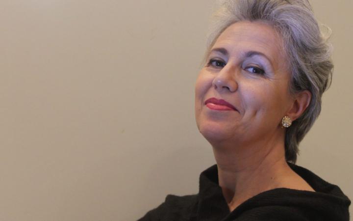Contralto with short silver-grey hair, red lips, and a black dress, portrayed in a three-quarter view with a serene gaze directed upwards against a neutral beige background