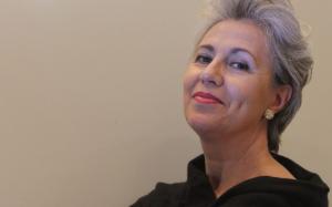 Contralto with short silver-grey hair, red lips, and a black dress, portrayed in a three-quarter view with a serene gaze directed upwards against a neutral beige background